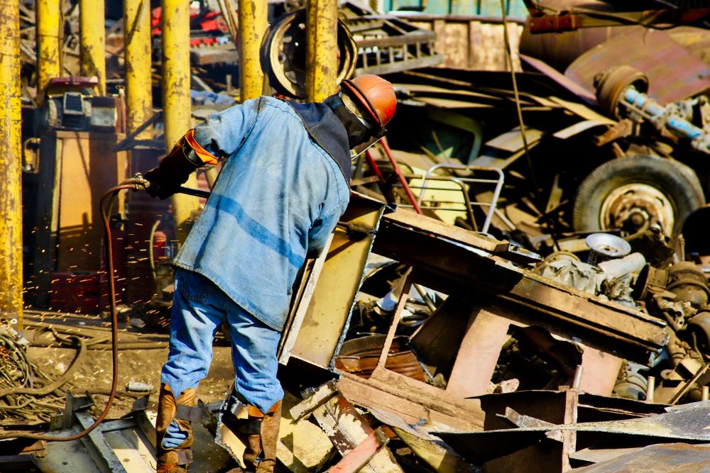 A man wearing a blue shirt and jeans is sorting through scrap metal at a construction site in San Francisco, CA.