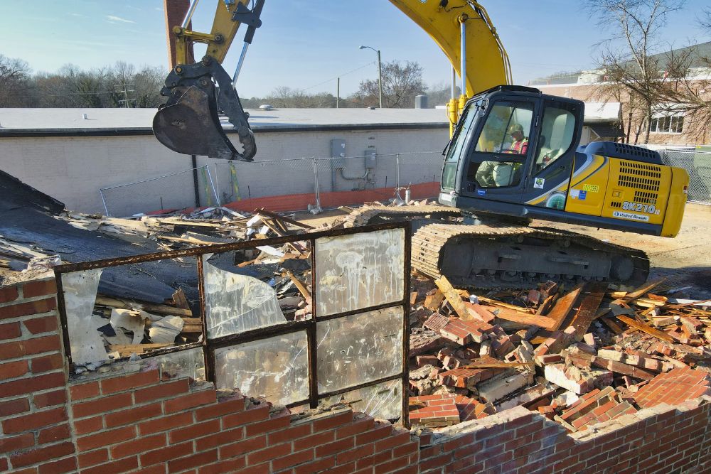 A bulldozer is actively tearing down a brick wall during a demolition service in San Francisco, CA.